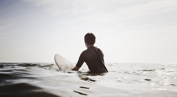 man in wet suit sits on a surfboard in the water