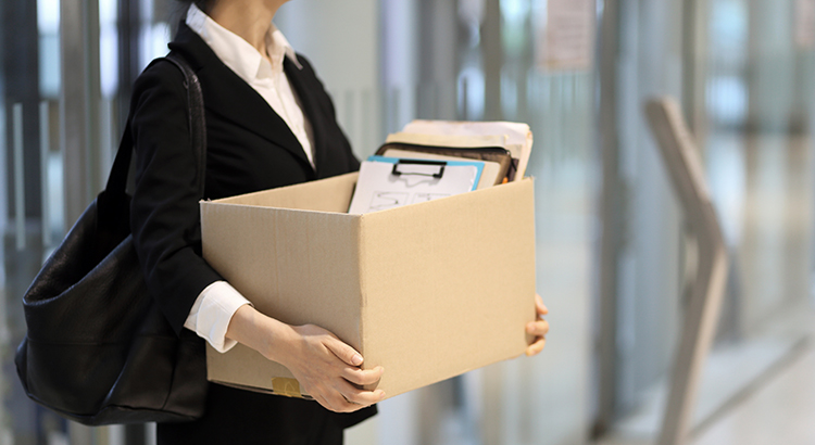 woman walking out of office with belongings in a cardboard box