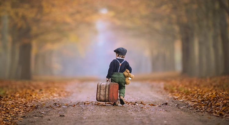 toddler boy from behind with suitcase and teddy bear in hands
