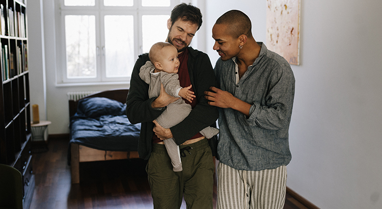 interracial gay male couple holding their baby