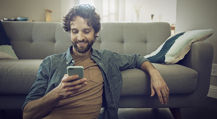 Smiling Man staring at phone sitting in front of couch on the floor